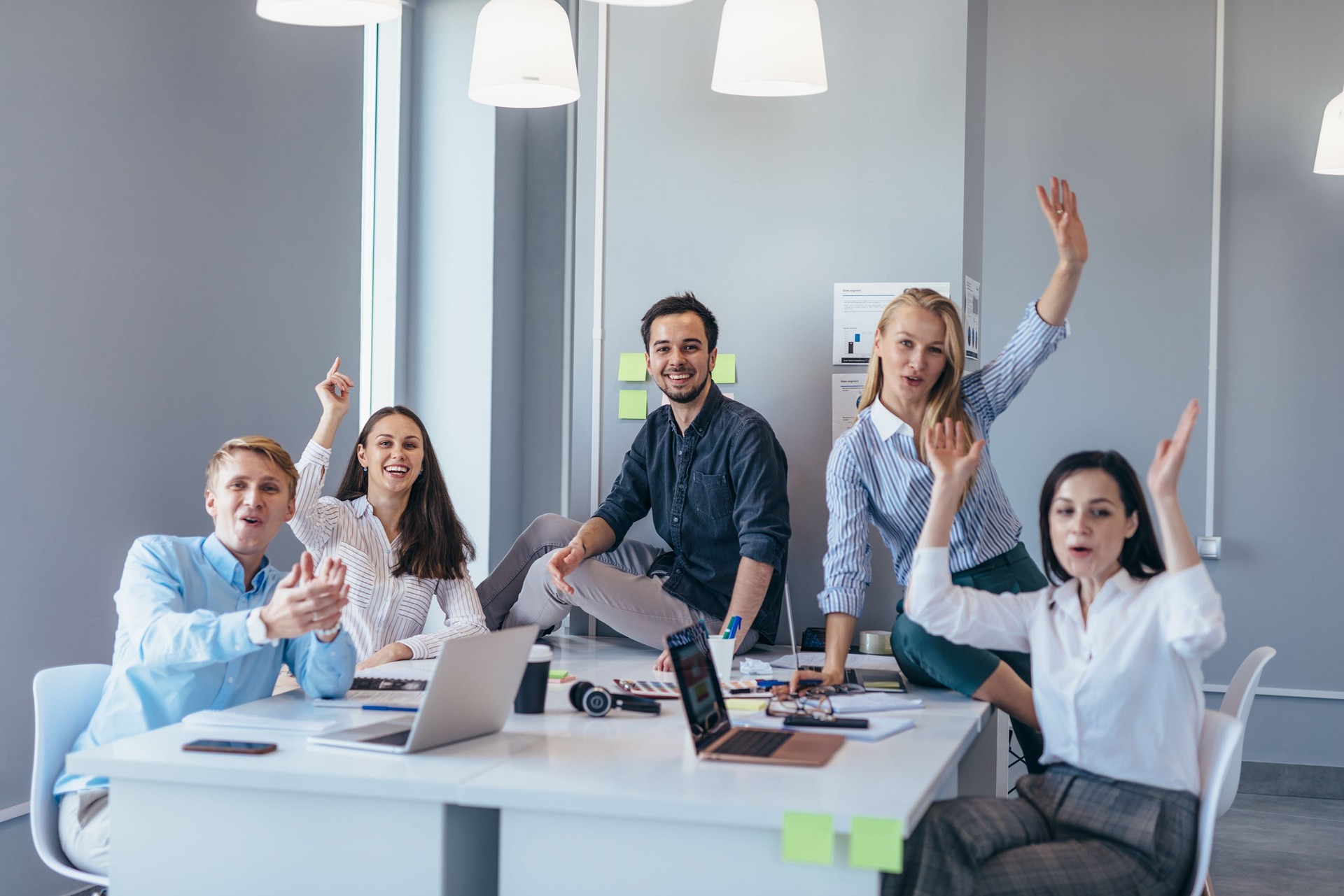 Group of young business people at a table waving their hands cheerfully as they look at the camera